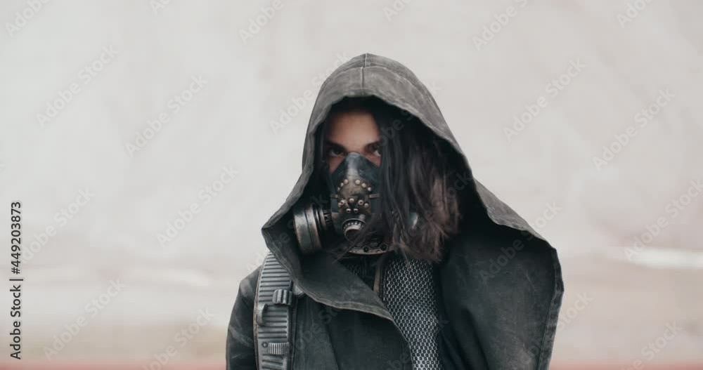 Portrait post apocalyptic woman in grunge clothes hooded mantle and protective gas mask standing by dunes in desert and looking into camera. Future female warrior survivor. Post apocalyptic world Portrait post apocalyptic woman in grunge clothes hooded mantle and protective gas mask standing by dunes in desert and looking into camera. Future female warrior survivor. Post apocalyptic world