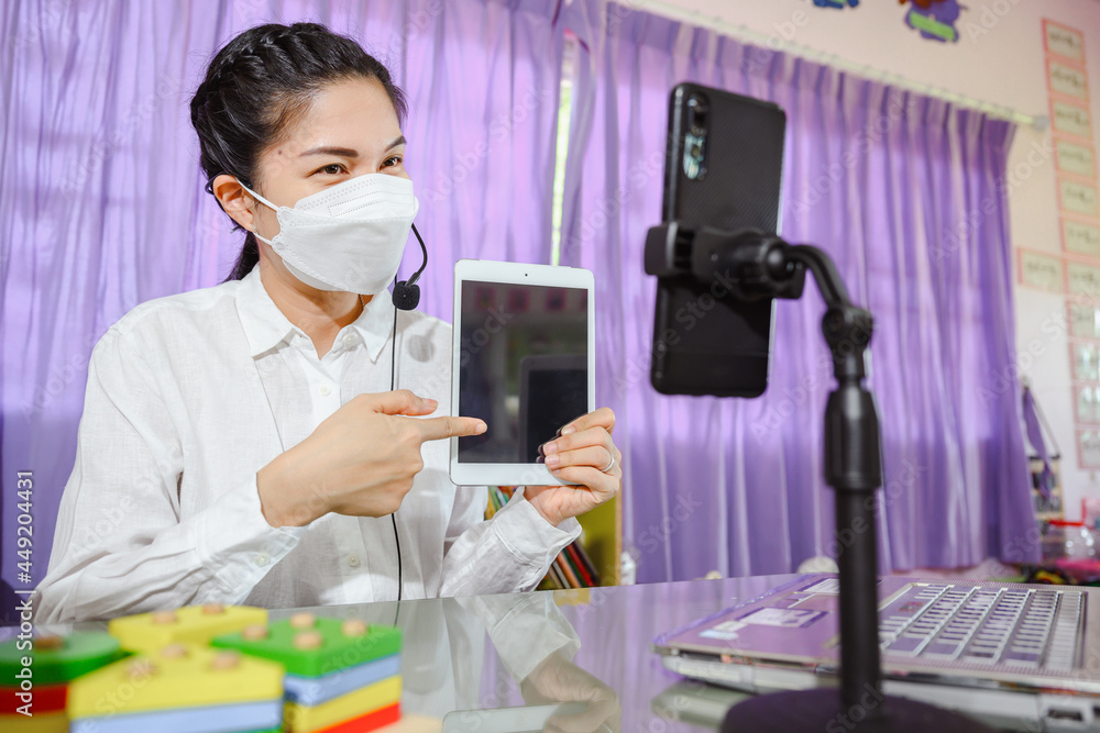 Asian female teacher wearing a mask is teaching students to study online through a computer screen by using an online video conferencing system for education Asian female teacher wearing a mask is teaching students to study online through a computer screen by using an online video conferencing system for education