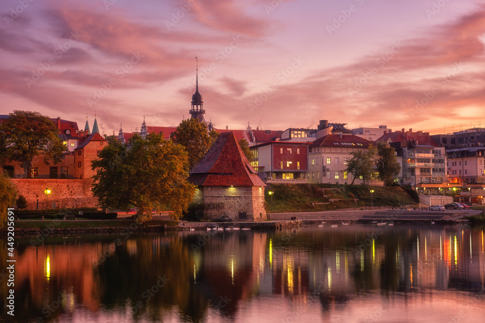 Amazing view of Maribor Old city, medieval water tower on the Drava river before sunrise, Slovenia. Scenic cityscape with cloudy sky and reflection, travel background for wallpaper or guide book