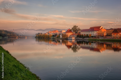 Amazing sunny and foggy morning  Maribor city on the Drava river  Slovenia. Scenic cityscape with buildings  reflection in the water  mountains on background and colorful sky