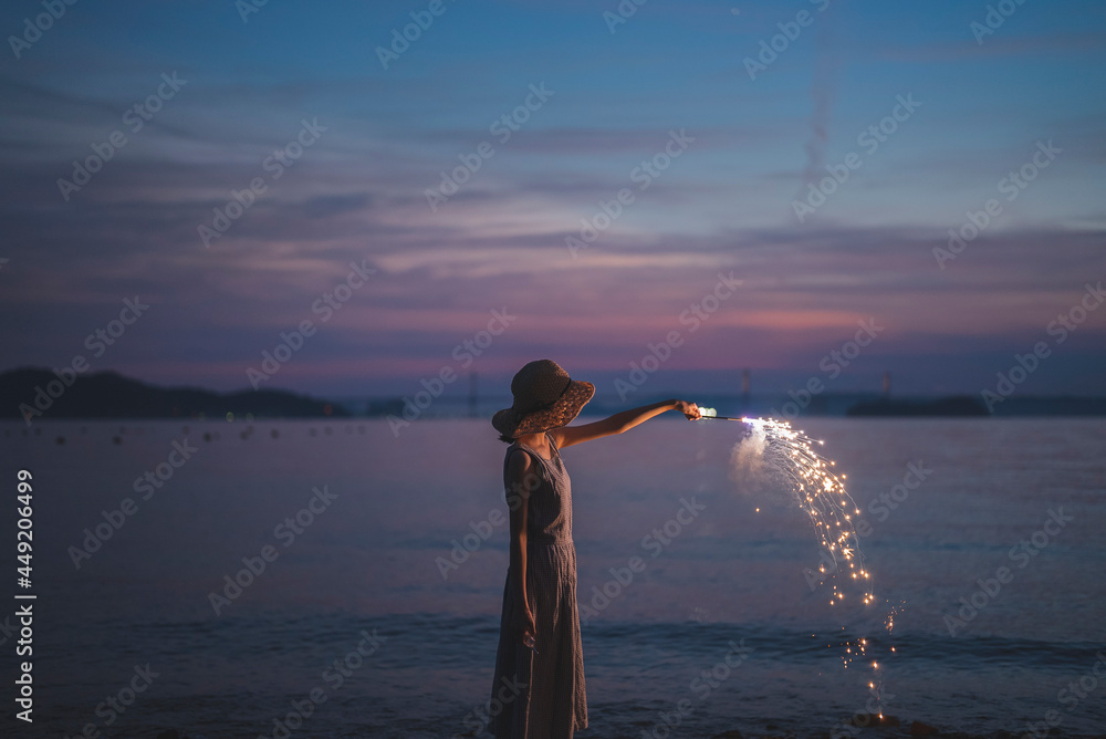 Fototapeta premium 夕暮れの海で花火をする女性