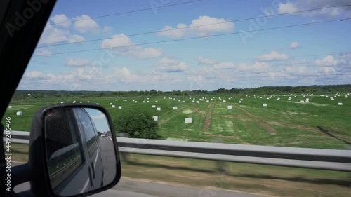 Round bales with silage wrapped in white plastic film on agriculture field view from car window photo