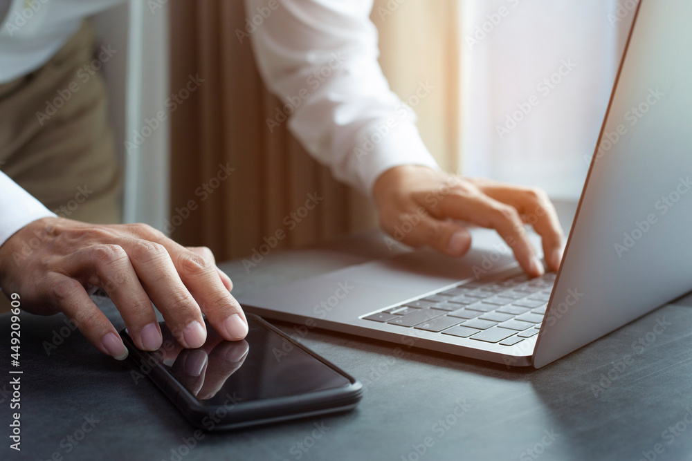 © kelvn - Man typing keyboard on laptop or computer and touch smart phone, closeup hands of businessman working at office