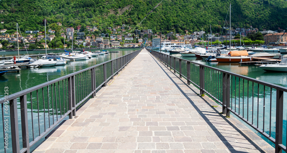 Obraz premium Gangway in the harbour of Como, Lake Como, Italy, On each side several boats and yachts are moored. Green hill on the background.