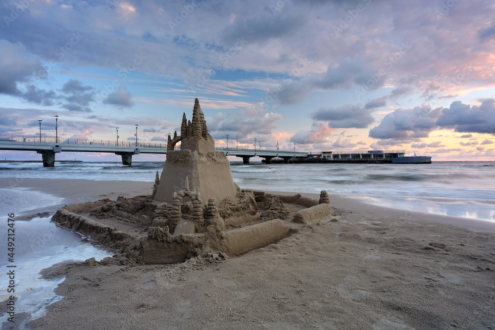 Zamek z piasku na plaży w Kołobrzegu, w pięknych barwach wschodzącego słońca.