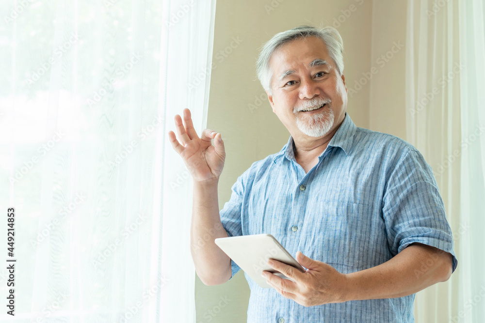 Senior Male using a smartphone and shows ok sign with hands, tablet computer , smiling feel happy in bedroom at home - lifestyle senior concept Senior Male using a smartphone and shows ok sign with hands, tablet computer , smiling feel happy in bedroom at home - lifestyle senior concept