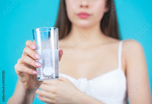 Young woman taking pill against headache. Brunette taking a pill with a glass of water. Woman taking drugs to releave headache. Brunette take some pills  holds glass of water  isolated on blue