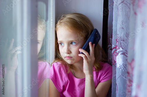 little girl in a pink dress speaks on the phone while sitting by the window, new technologies