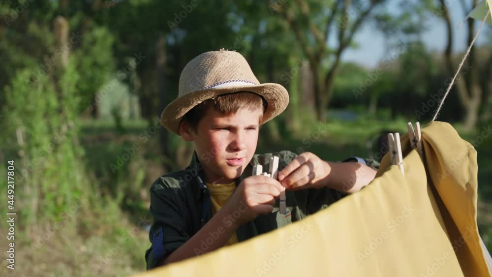 childhood, cute little boy in straw hat build wigwam and clings clothespins to fabric during summer vacation in countryside childhood, cute little boy in straw hat build wigwam and clings clothespins to fabric during summer vacation in countryside