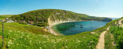 Obraz na plátně Lulworth cove with the SW coastal path on the hilltop on a bright summer's day with grass and flowers leading down to the beach