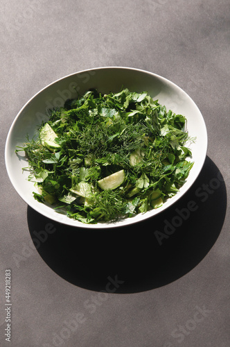 Salad with dill and parsley cucumbers on a white plate stands on a gray background.