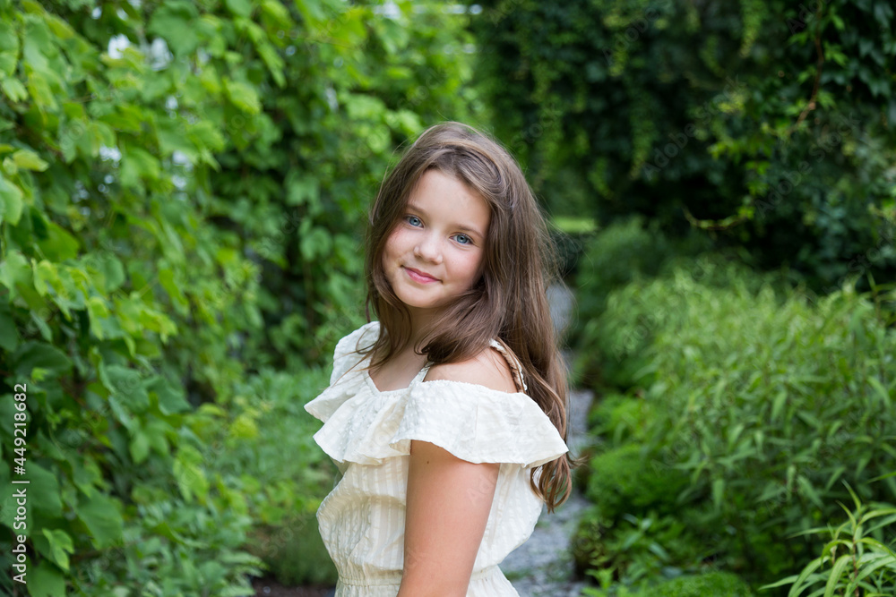Selective focus medium portrait of gorgeous smiling young girl in summer dress posing against green foliage background, Quebec City, Quebec, Canada