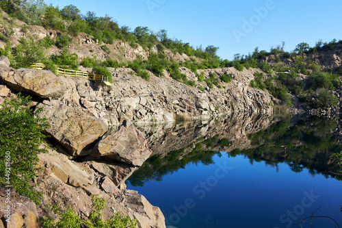 Mountain lake in the summer. Panoramic view on old flooded granite quarry with radon water. Landscape with rock stones, green trees and clean pond
