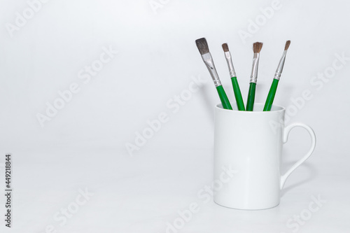 Paint brushes kept inside a white ceramic mug holder 