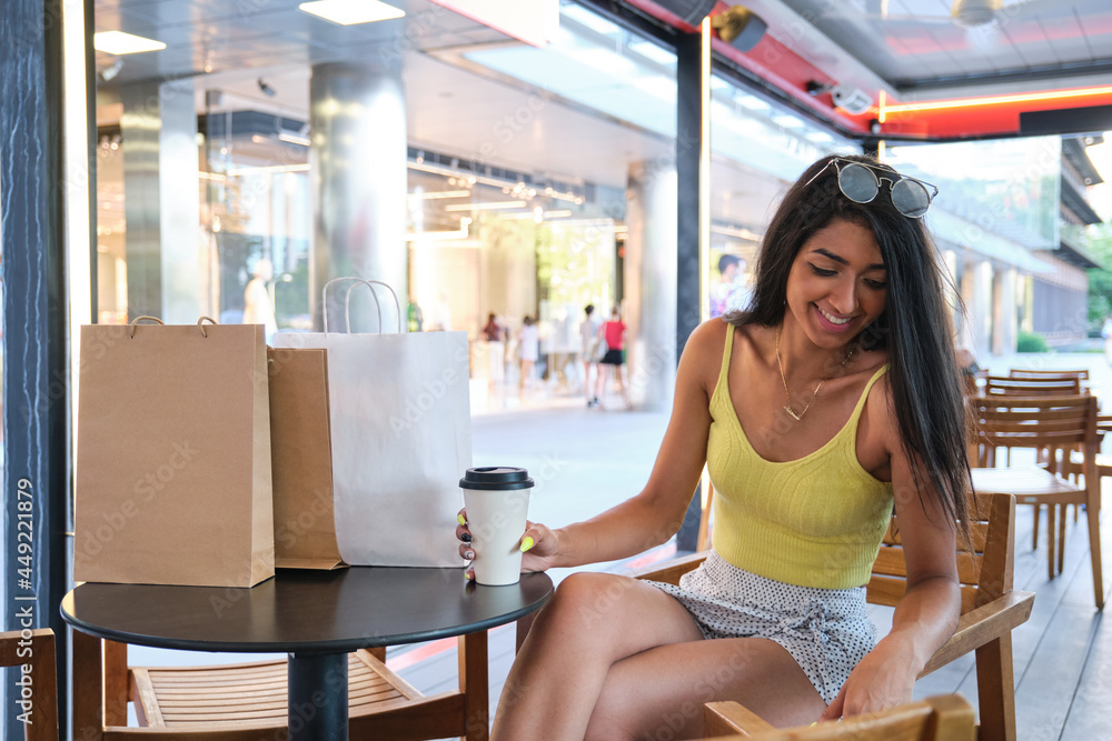 Young latin woman drinking a coffee at a coffee shop after going shopping.