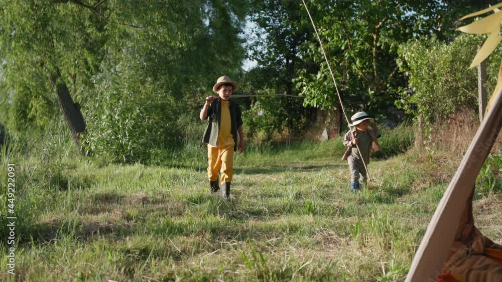 children in countryside, cute boys in hats with fishing rods in their hands have fun relaxing on lawn by the river among trees children in countryside, cute boys in hats with fishing rods in their hands have fun relaxing on lawn by the river among trees