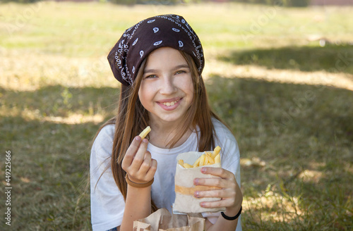 A teenage girl is sitting in a clearing and eating French fries. Close-up portrait photo