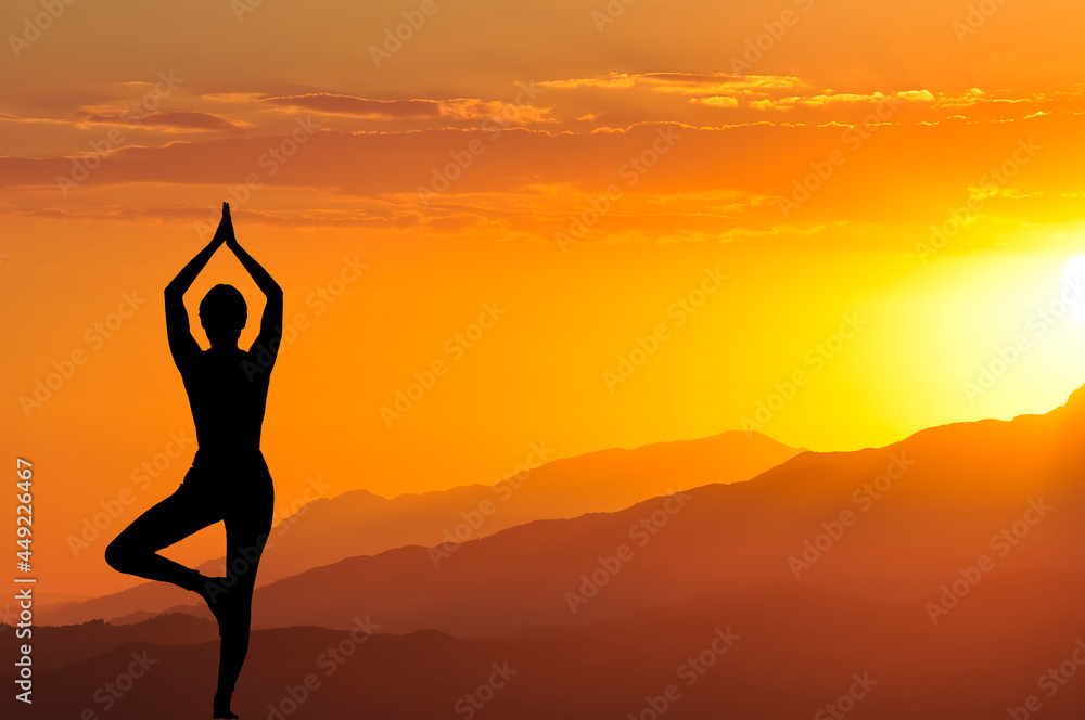 the silhouette of a girl meditating in a yoga pose standing with her hands raised up against the background of a beautiful sunset in the mountains