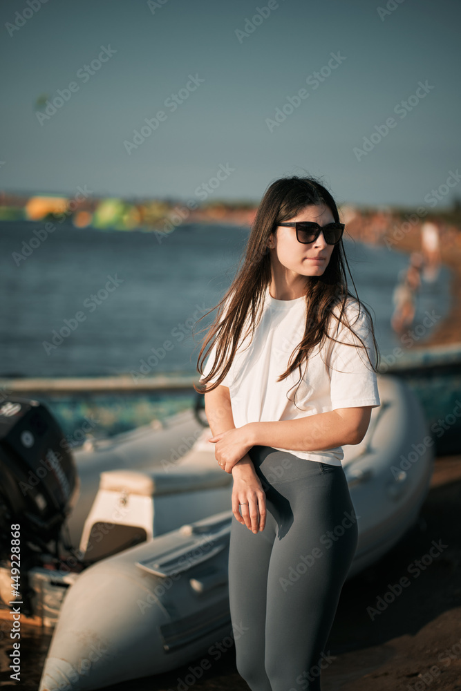 Young woman on the beach with long hair. Fit beautiful girl wears white shirt and gray leggings on the beach