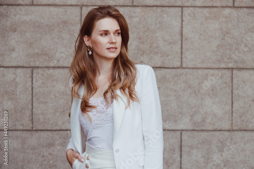 Confident elegant woman in white blazer outdoors looking away. Business style.