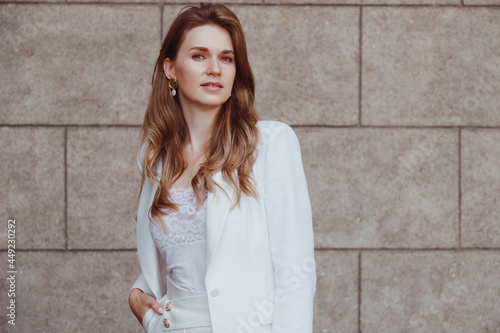 Confident elegant woman in white blazer outdoors looking away. Business style.
