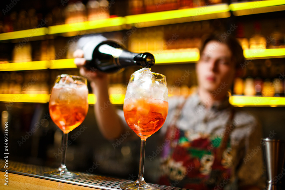 bartender pours orange sparkling wine and aperol cocktail with ice on bright yellow bar counter