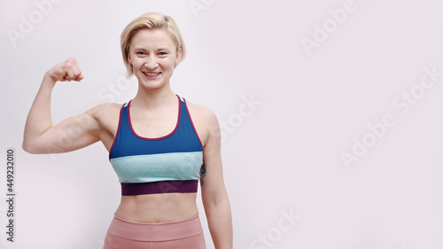 Girl dressed in activewear showing her biceps. Strong girl posing for the camera showing her muscles and strength. Concept of fitness and gym. Isolated over white background studio.