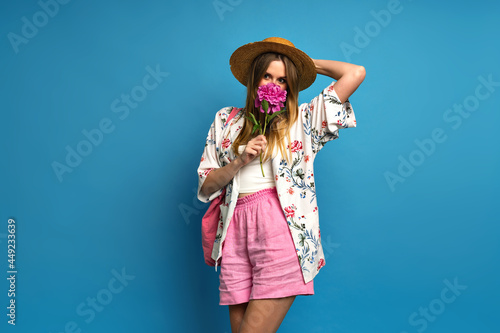 Studio portrait of happy blonde woman posing with peony flower, romantic atmosphere summer vacation.