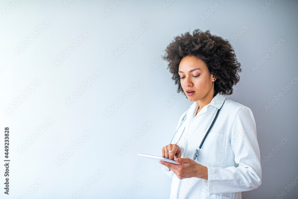 Doctor with digital tablet. Attractive young female doctor in white lab coat working on digital tablet and smiling while standing against grey background Doctor with digital tablet. Attractive young female doctor in white lab coat working on digital tablet and smiling while standing against grey background