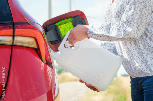 Close up woman refilling the red car with fuel or a diesel engine fluid from canister in the field. 