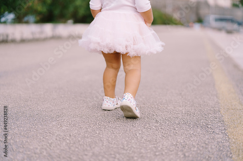 Legs of a little girl in a fluffy skirt stand on the asphalt road