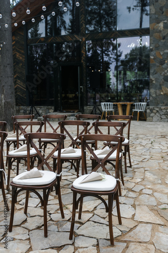 brown wooden chairs with crisscross back. White pillows on chairs and envelopes with white rose petals. against the backdrop of nature on a stone floor. holiday concept.