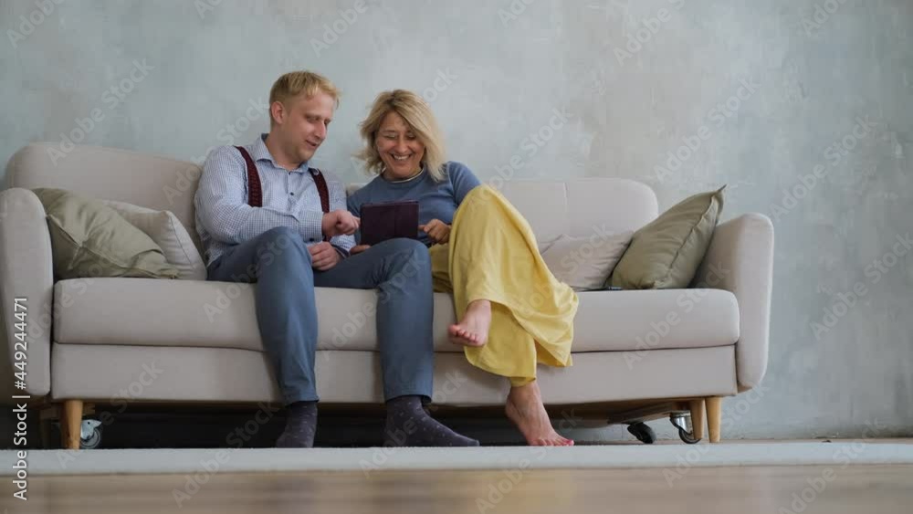 Male with his Mature Mother Playing Online Games on Tablet PC while Sitting on the Sofa in the Living Room. Bonding and Family Reunion, Mothers Day Concept Male with his Mature Mother Playing Online Games on Tablet PC while Sitting on the Sofa in the Living Room. Bonding and Family Reunion, Mothers Day Concept