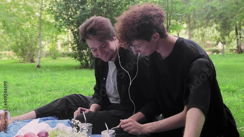 Two young guys in love listen to music in nature in the summer