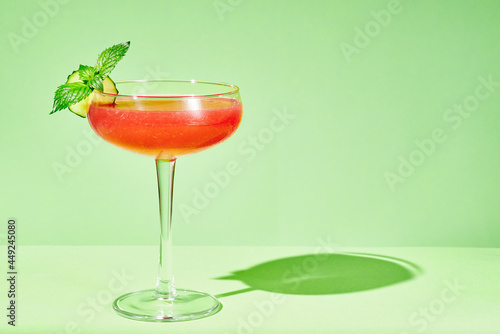 Watermelon cocktail with  cucumber slice and mint leaves in a coupe glass on a green .