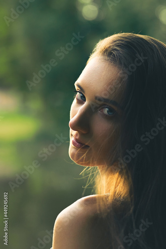 Gorgeous young brunette woman portrait during golden summer sunset in blurred nature background