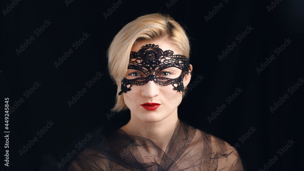 Fototapeta premium A blonde model dressed in a masquerade ball costume for the fancy costume party. Wearing A Venetian Masquerade Mask and red lipstick. Closeup headshot. Mysterious girl wearing a Masquerade mask.
