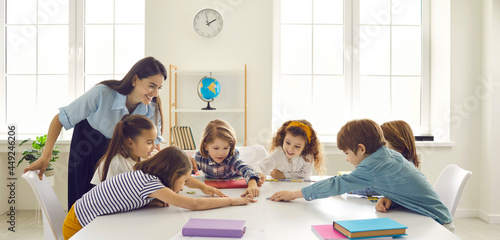 Quadro em tela Female teacher and pupils group playing funny educational game at table desk in classroom