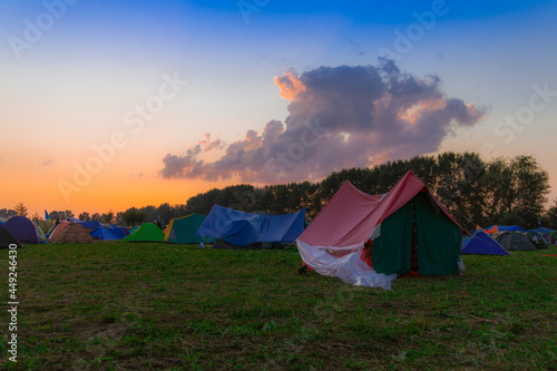 festival camp tent together with a lot of people on evening meadow landscape with beautiful blue and orange colors on sky with one cloud  life style photography concept