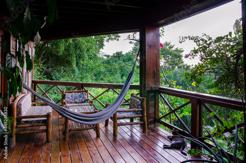 Tree cabin porch with hammock and sitting area with jungle views in Roatan. Ecofriendly hostel with rustic outdoor balcony with tree forest in the background. Relax and nature vacation