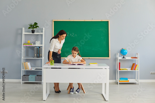 Friendly school teacher helping little pupil with math assignment in modern classroom