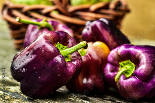fresh whole purple bell peppers on rustic wood tabletop with woven wicker basket
