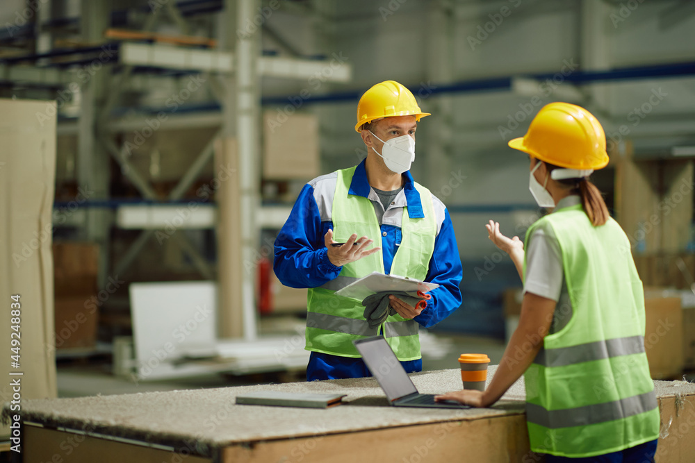 Warehouse worker discusses with female colleague while working in storage room during coronavirus pandemic. Warehouse worker discusses with female colleague while working in storage room during coronavirus pandemic.