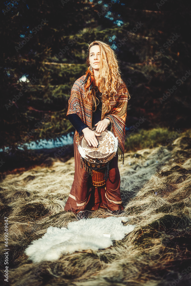beautiful shamanic girl playing on drum in the nature.