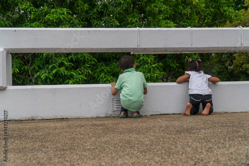 Little asian kids stand on the bridge, leaning on the fence.