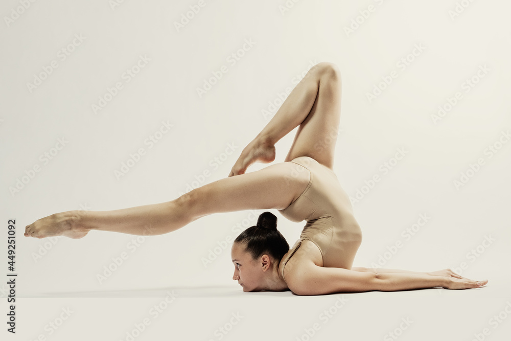 gymnast performs exercise miracles of flexibility stand on the shoulders with a bend in the back in a beige leotard on a white background
