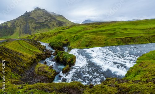 Panorama of scenic high mountain Drangshildarfjall over Skogafoss waterfall among green field in the south of Iceland