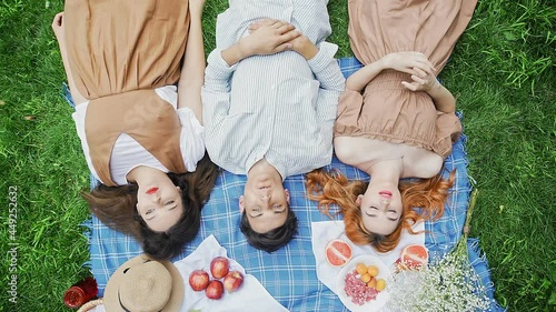 A guy and two girls in the summer lie on a blanket in nature and communicate top view
