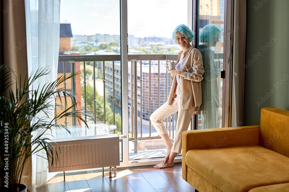 Excited caucasian woman with coloured blue hait posing on balcony, with cup of tea, enjoying morning alone at home, in casual domestic clothes, relaxed and dreamy. side view portrait, copy space Excited caucasian woman with coloured blue hait posing on balcony, with cup of tea, enjoying morning alone at home, in casual domestic clothes, relaxed and dreamy. side view portrait, copy space