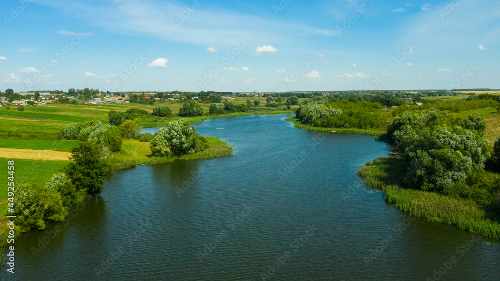 Aerial view of the river surrounded by green fields through which the river flows. Rural landscape in the countryside.